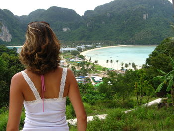 Rear view of woman looking at beach against mountains