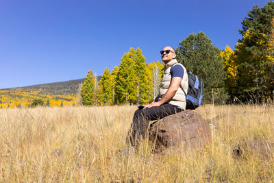 Happy smiling man takes a rest during hiking in mountains at fall season on sunny day. male hiker