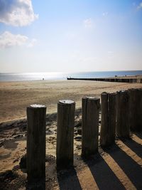 Wooden posts on beach by sea against sky