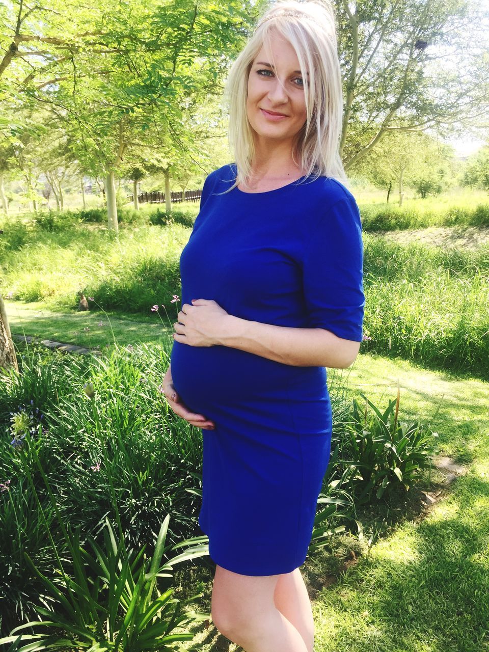 looking at camera, portrait, pregnant, blond hair, one person, mother, green color, growth, standing, only women, day, smiling, happiness, one woman only, real people, new life, beautiful woman, tree, adult, adults only, people, outdoors