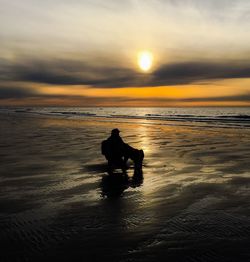 Silhouette people on beach against sky during sunset