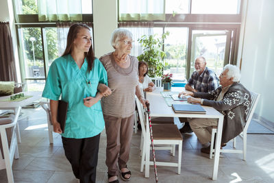 Young nurse and senior woman walking arm in arm at nursing home