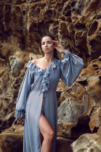 Fashionable brunette woman in a gray dress stands on a cheese rock in the summer