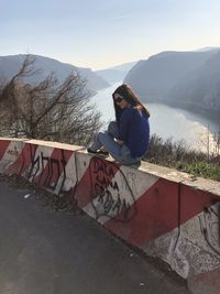 Woman sitting on retaining wall against mountain