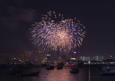 Firework display in city against sky at night