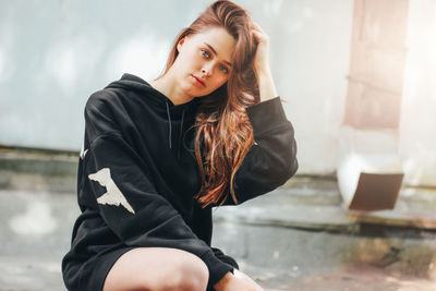 Portrait of beautiful young woman with hand in hair crouching against wall