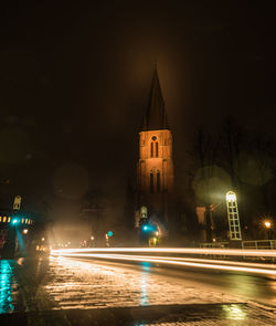 Light trails on road by illuminated buildings at night