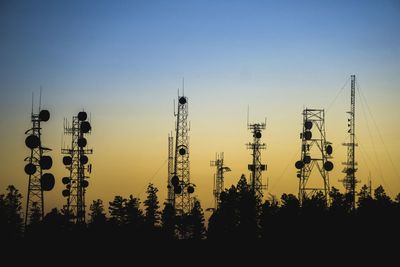 Silhouette trees and radio towers against sky during sunset