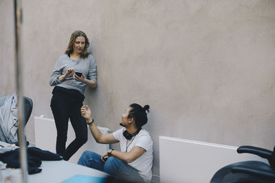 Male computer programmer talking to female colleague holding smart phone in office