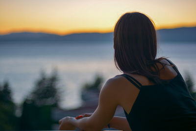 Rear view of woman looking away while sitting outdoors during sunset