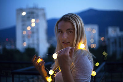 Close-up of young woman holding illuminated lighting equipment at night