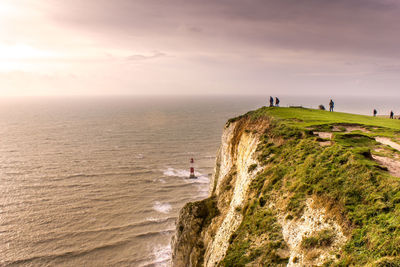 People on cliff by sea against sky during sunset