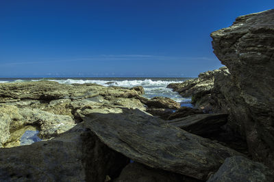 Rock formations on shore against blue sky