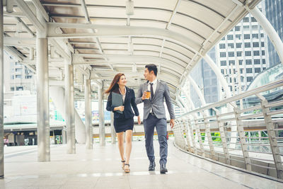 Smiling colleagues walking on elevated walkway in city