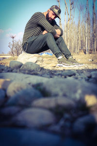 Side view of young man sitting on rock