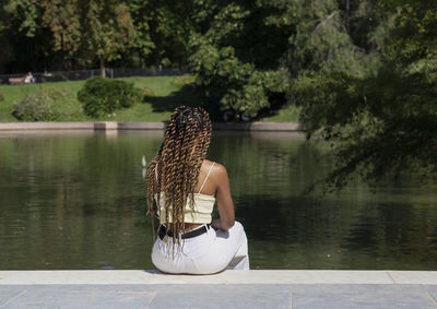 Rear view of woman sitting by lake against trees