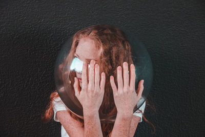 Young woman wearing glass container against black background