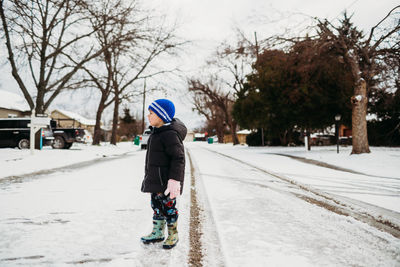 Young boy standing in snowy road wearing jacket in winter