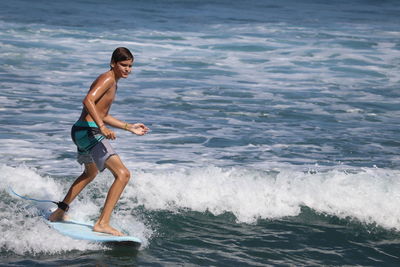 Full length of shirtless boy surfing in sea