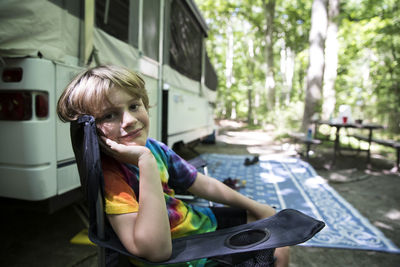 Young boy in tie dye shirt sits in camping chair in front of pop up