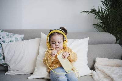 Baby girl putting headphones in mobile phone on sofa