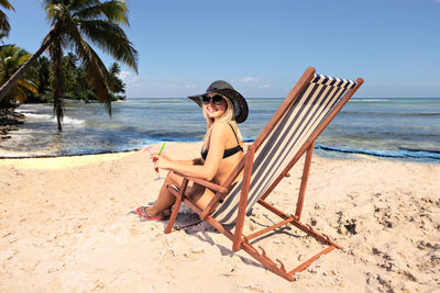 Portrait of woman sitting on chair at beach against sky