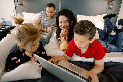 Parents and girl with boy using laptop on bed in hotel room