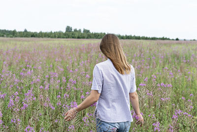 Rear view of young blond woman  standing in field among flowers of fireweed, beauty in nature 