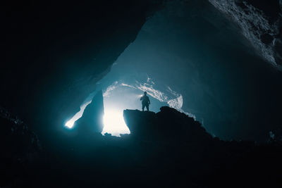Low angle view of silhouette man standing on rock in cave