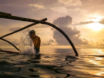 Man bathing in sea against sky during sunset