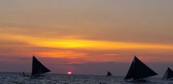 Silhouette sailboat sailing on sea against orange sky