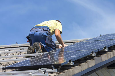 Low angle view of people working on roof against sky