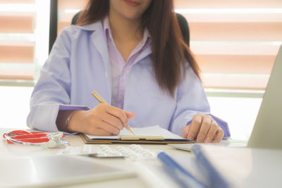 Midsection of woman using mobile phone while sitting on table