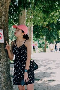 Young woman wearing hat standing against tree