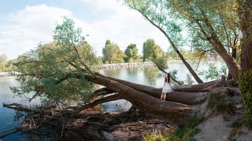 Woman sitting on fallen tree at riverbank