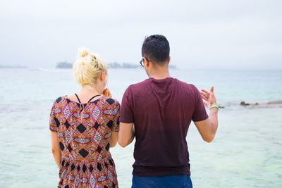 Rear view of couple standing at beach against sky