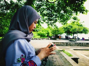 Profile view of young woman using phone while sitting at park