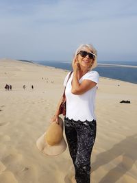 Portrait of woman wearing sunglasses while standing at beach against sky