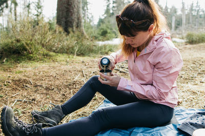 Young beautiful woman drinking hot tea or coffee from a thermos in the forest on a walk. hiking