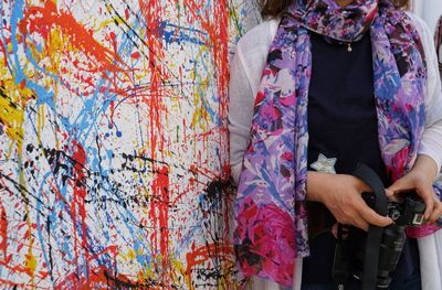 Midsection of woman holding camera standing against colorful wall