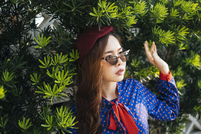 Portrait of young woman wearing sunglasses against plants
