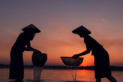 Silhouette people standing by lake against sky during sunset