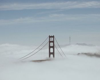 Low angle view of suspension bridge against cloudy sky