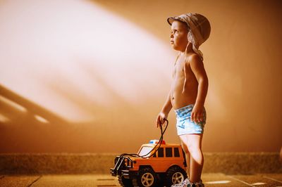 Side view of boy standing with toy car against wall