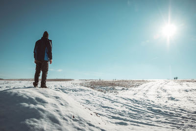 Rear view of man standing on snow covered landscape against blue sky