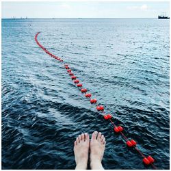 Low section of woman dangling feet over sea