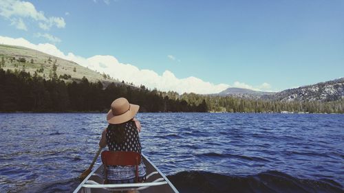 Rear view of woman sailing boat on lake against sky