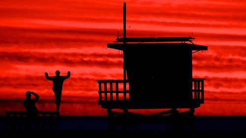 Silhouette man standing by sea against orange sky