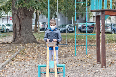 Pensive boy wearing face mask while playing alone at the playground.