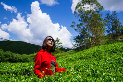 Young woman looking away on field against sky